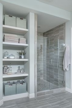 a walk in shower sitting next to a white shelf filled with towels and other items