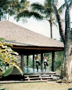 two people are doing yoga in front of a wooden structure with trees and grass around it