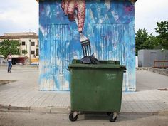 a green trash can sitting in front of a blue wall with a painting on it