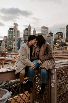 two people sitting on top of a metal fence in front of a cityscape