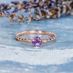 a close up of a ring with a purple stone on it and lavender flowers in the background