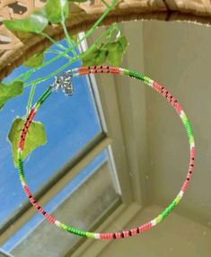 a green and red beaded necklace hanging from a window sill in front of a blue sky