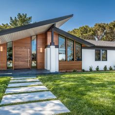 a modern house in the middle of a grassy area with stepping stones leading up to it's front door