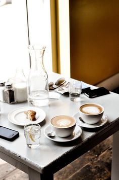 the table is set with two cups and saucers on it, next to a cell phone