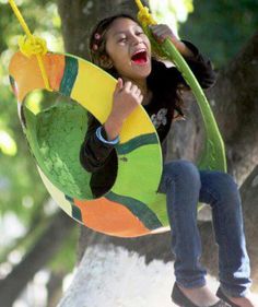 a woman is sitting on a tree swing and laughing while holding onto the handle with both hands