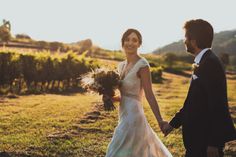 a bride and groom holding hands walking through the grass