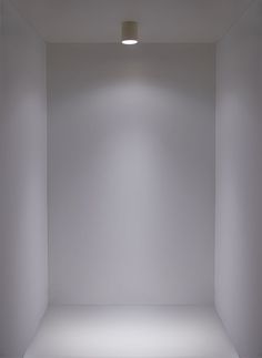 an empty white room with light coming in from the ceiling and lights on either side