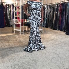 a woman standing in front of a rack of clothes at a clothing store wearing a black and white dress