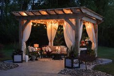 an outdoor gazebo with lights on the top and curtains hanging over it's sides