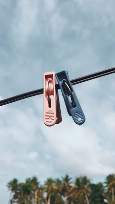 two pairs of pink and blue scissors hanging on a wire with palm trees in the background