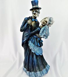 a skeleton figurine with a blue dress and top hat holding a baby doll