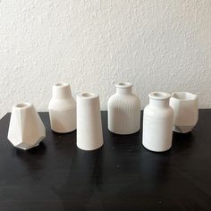 five white vases sitting on top of a black table