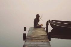 a woman sitting on the end of a dock next to a boat