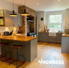 an open kitchen with wooden floors and gray cabinets, along with two bar stools