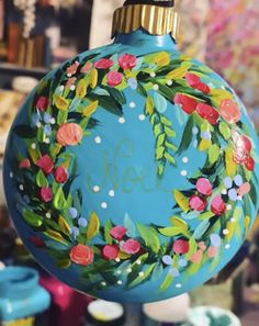 a blue ornament with flowers painted on it's side and the word noel in gold lettering