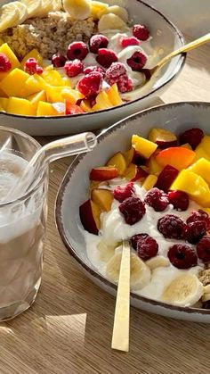 two bowls filled with fruit and yogurt on top of a wooden table next to a glass of milk