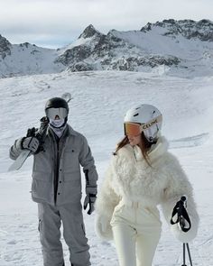 a man and woman walking in the snow with skis on their feet while holding hands