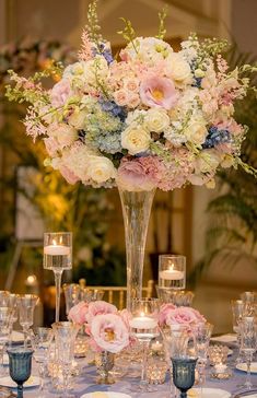 a tall vase filled with lots of flowers on top of a table covered in candles