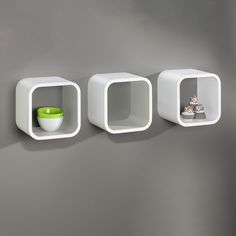 three white shelves on the wall with one green bowl and two empty ones in it