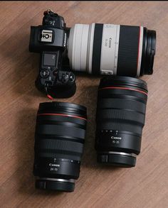 three cameras sitting next to each other on top of a wooden table with two lenses