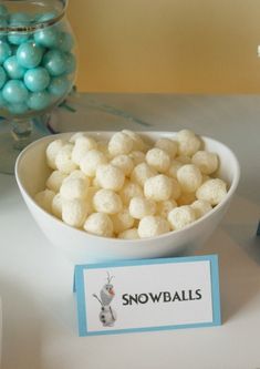 a bowl filled with snowballs sitting on top of a table next to blue and white candies