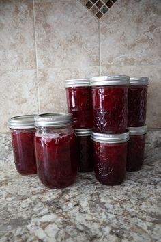 jars of cherry jam are stacked on top of each other in front of a tile wall