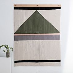 a wall hanging on the side of a white wall next to a potted plant