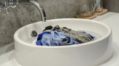 a white sink with clothes in it next to a toothbrush