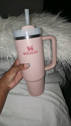 a person holding a pink starbucks cup on top of a white bed with fluffy pillows