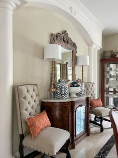 a living room filled with furniture next to a tall white columned wall in front of a mirror