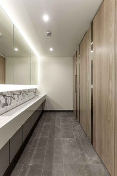 a long bathroom with marble counter tops and wooden cabinets on either side of the sinks