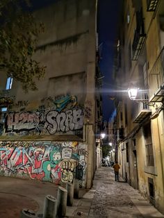 an alleyway with graffiti on the walls and in between two buildings, at night