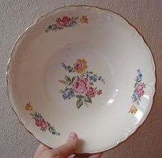 a hand holding a white bowl with flowers on it