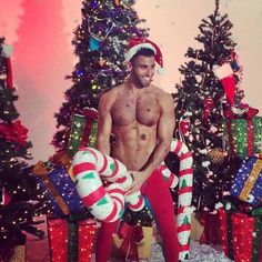 a shirtless man standing in front of christmas trees with presents and gifts around him