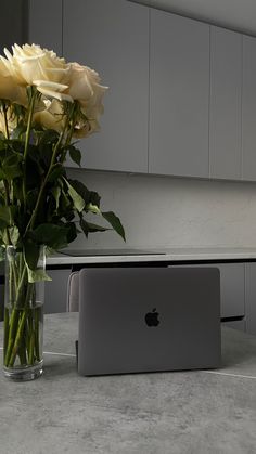 a bouquet of roses in a vase next to an apple laptop on a kitchen counter