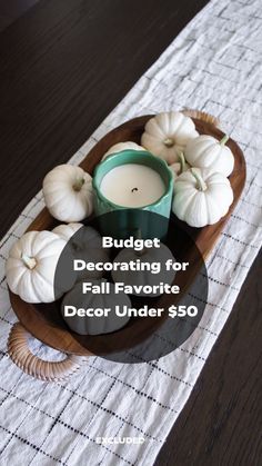 a wooden plate topped with white pumpkins next to a candle on top of a table