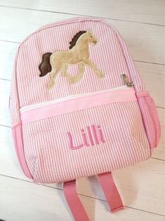 a pink and white backpack with a horse embroidered on the front, sitting on a wooden floor