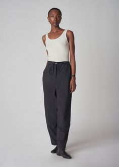 Elevated jogger pant with drawstring, metal snap closure and center front zip. Featuring turn back self waist, back flap pockets, and tonal knee patches. Bias binding finish. Details 100% Nylon 5127LWN-PS24 Black Relaxed fit. 28" inseam across all sizes. Model is 5'10" and wears a size Small. Outfit Flat Lay, Knee Patches, Bias Binding, Drawstring Jogger, Exclusive Dress, Hooded Parka, Denim Shoes, Cotton Viscose, Drawstring Pants