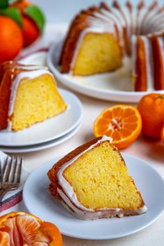 slices of orange cake on white plates with silverware next to them and an orange in the background