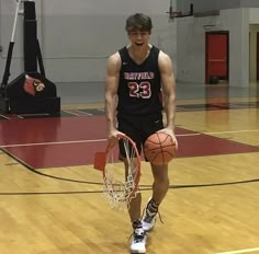 a young man holding a basketball on top of a basketball court with a hoop in his hand