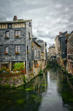 a river running through a small town next to tall buildings with flowers growing on the windows