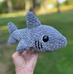 a hand holding up a gray knitted shark toy with black eyes and teeth,