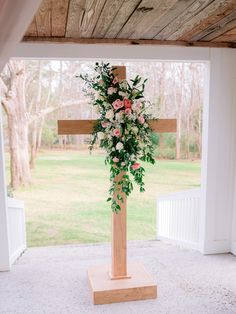 a wooden cross with flowers on it sitting in front of a door way that leads to a grassy field