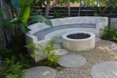 a circular bench sits in the middle of a graveled area surrounded by trees and plants