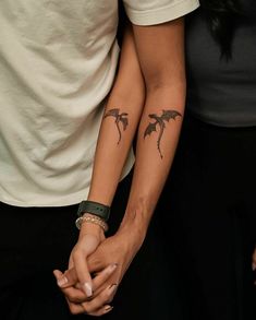 two people holding hands with tattoos on their arms