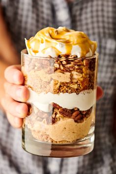 a person holding a glass filled with desserts and whipped cream on top of it