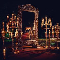 an elaborately decorated mirror and candles stand in the middle of a garden at night