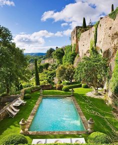 an outdoor swimming pool surrounded by greenery and stone walls in the middle of a garden