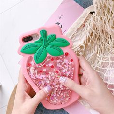 a person holding a pink phone case with glitters and a green leaf on it