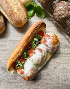 a meatball sub sandwich with tomato sauce and cheese on it next to some bread rolls